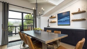 A modern dining area with a large table, leather chairs, and a view through a large window.