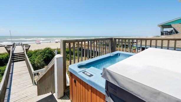 En træterrasse, der fører til en jacuzzi med udsigt over stranden og havet.