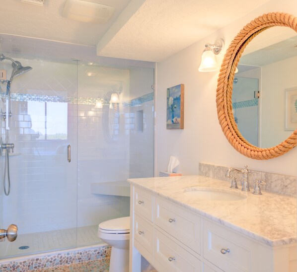 A bathroom with a glass-enclosed shower, a marble sink, and a large mirror with a rope frame.