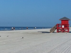 A beach with a red lifeguard tower, clear skies, and people walking along the shore.