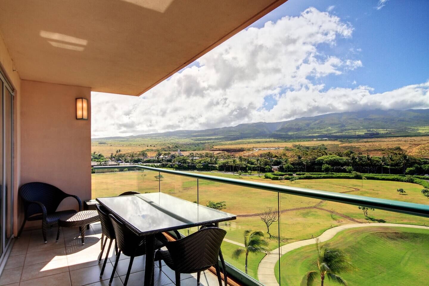 A balcony with a table and chairs, offering a view of a green landscape with hills and a clear sky.