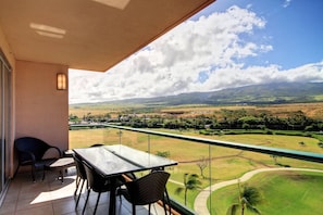 A balcony with a table and chairs, offering a view of a green landscape with hills and a clear sky. - KLVR presents Honua Kai K612*Two bedrooms*one bath (Lahaina)