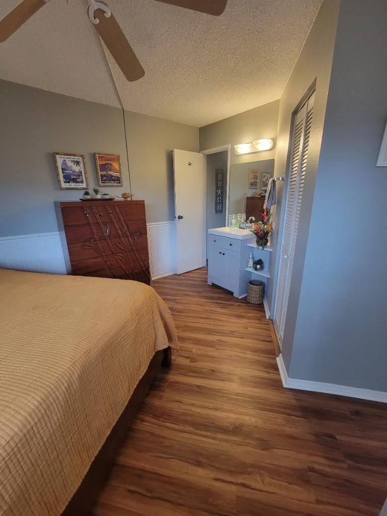 A bedroom with a bed, wooden flooring, a ceiling fan, a dresser, and a vanity with a mirror.
