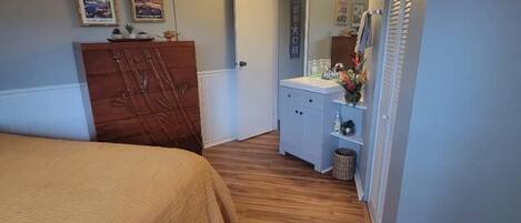 A bedroom with a bed, wooden flooring, a ceiling fan, a dresser, and a vanity with a mirror.