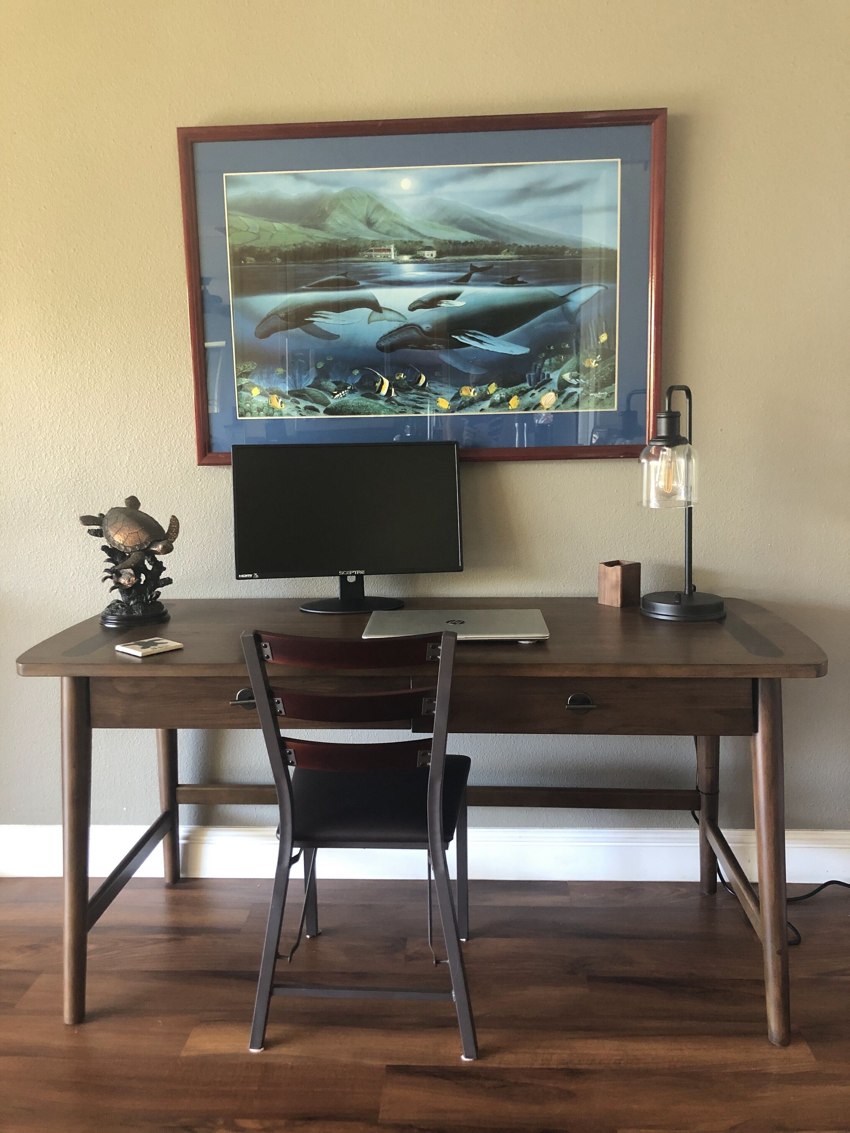 Un escritorio de madera con un monitor de computadora, una laptop y un cuadro con vida marina.