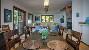 Un coin repas avec une table en bois, des sets de table en fibres tressées et un vase de fleurs.