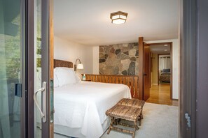 Une chambre à coucher avec un lit, un mur en pierre, un banc en bois et une porte donnant sur une autre pièce.