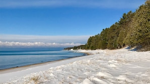 Une plage enneigée, avec un ciel dégagé et une zone boisée en arrière-plan.