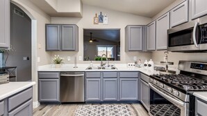 A modern kitchen with grey cabinets, stainless steel appliances, and a central island. - 5 Star Oasis ~ Pool w/ Waterfall, Hot Tub, EV Charger & Family Comfort (Mesa)
