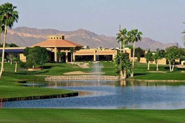 Un parcours de golf avec un étang, des palmiers et un bâtiment doté d’un toit rouge.
