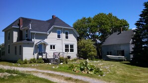 Une maison à deux étages avec un porche à l’avant, un bateau garé dans l’allée et un grand arbre en arrière-plan.