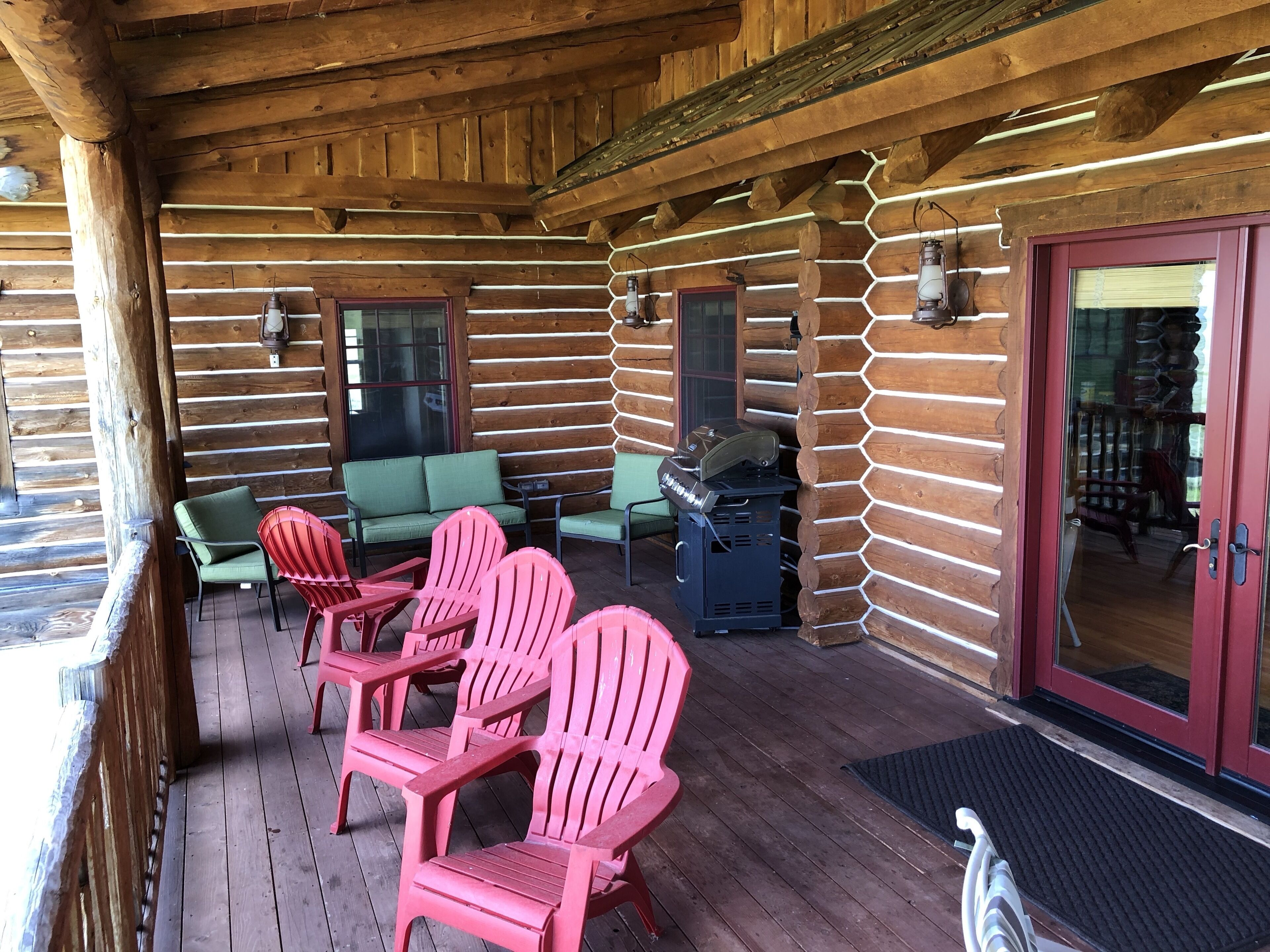 Une cabane en rondins dotée d’une terrasse en bois, d’un espace extérieur aménagé avec des chaises et d’un coin barbecue.