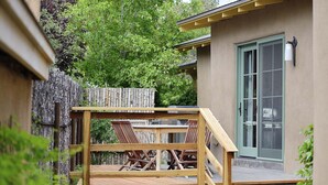Un patio in legno con mobili da esterno, una recinzione di legno e un edificio con una porta e una finestra verde.