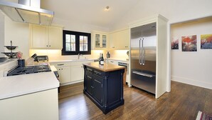 Una cucina moderna con mobili bianchi, un'isola centrale, un frigorifero in acciaio inossidabile e una finestra con cornice nera.