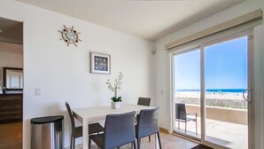 A dining area with a white table, four chairs, a potted plant, a trash bin, and a view of the beach through a sliding glass door. - 50' of Ocean Front * Exclusive Ground Level Patio * AC (San Diego)