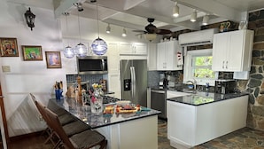 A kitchen with a central island, white cabinets, a stone backsplash, and various appliances. - The Beach House on St. Thomas with Secluded Sand Beach (St. Thomas)