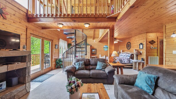 Ein Holzhütten-Interieur mit Kamin aus Stein, einer Couch, einem Couchtisch und einer Treppe, die zu einer oberen Ebene führt.
