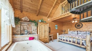 Ein Schlafzimmer in einer Blockhütte mit einem großen hölzernen Bett, einem Holzschrank, einem kleinen Holzstuhl, einem Kamin aus Stein und einer großen Badewanne.