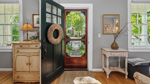 A room with a wooden cabinet, a dark door with a glass panel, a small white table with a vase, and a window with a view of greenery. - Private Hot Tub/Short Walk to Downtown (Napa)