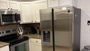 Una cocina moderna con armarios blancos, electrodomésticos de acero inoxidable, incluyendo un refrigerador, horno y microondas, y una encimera de granito.