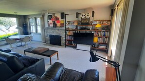 A modern living room with a sofa, a coffee table, a fireplace, a bookshelf, and a television. - Beautiful Lake Front Home On Como with boat and motor included (Lake Geneva)