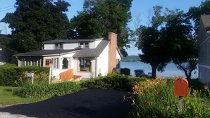 A two-story house with a brick chimney, a mailbox, and a view of a lake. - Beautiful Lake Front Home On Como with boat and motor included (Lake Geneva)