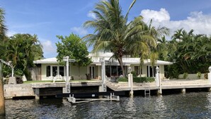A waterfront property with a dock, a covered seating area, and lush greenery.