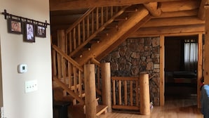 Una scala in legno con una parete in pietra sullo sfondo, una parete bianca con un termostato e una presa di corrente.