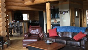 Interno di una baita di legno con un soggiorno che presenta un divano in pelle marrone, un tavolino da caffè e un camino.