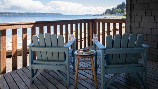 Two Adirondack chairs on a wooden deck with a view of the beach and ocean.
