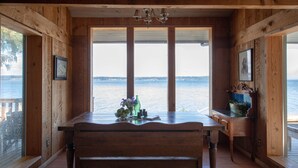 A wooden interior with a large table and bench, a view of the water, and a chandelier.