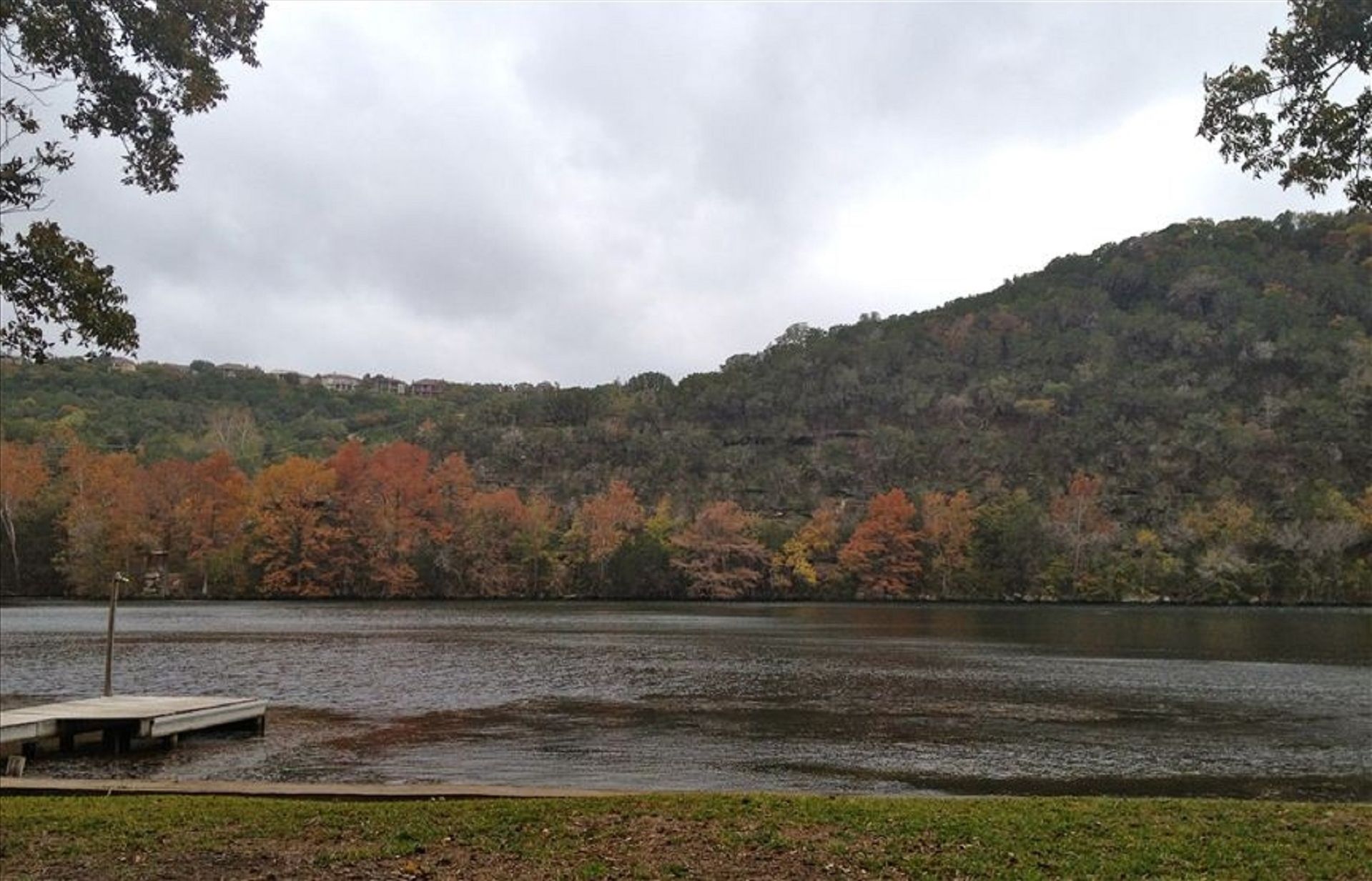 Vista del lago con un muelle, árboles de colores otoñales y una colina al fondo.