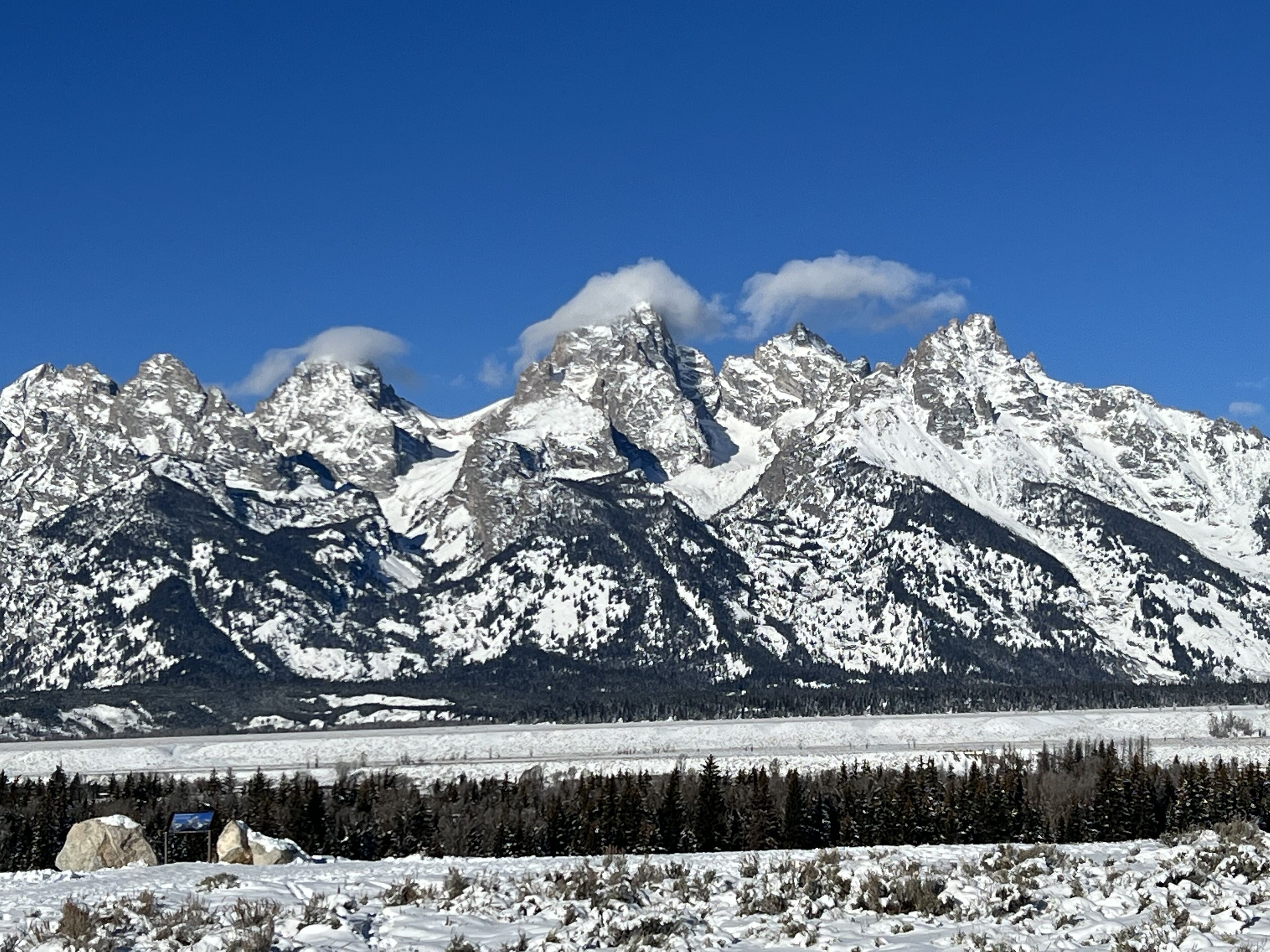 Een berglandschap met besneeuwde toppen en een helderblauwe lucht.