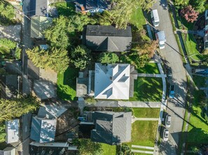 Ett flygbildsbild av ett bostadsområde med flera hus, en central byggnad med ett karakteristiskt tak och en gata med parkerade bilar.