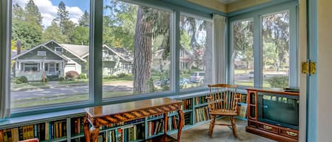 Une véranda avec de grandes fenêtres, une bibliothèque en bois, un téléviseur et un fauteuil.