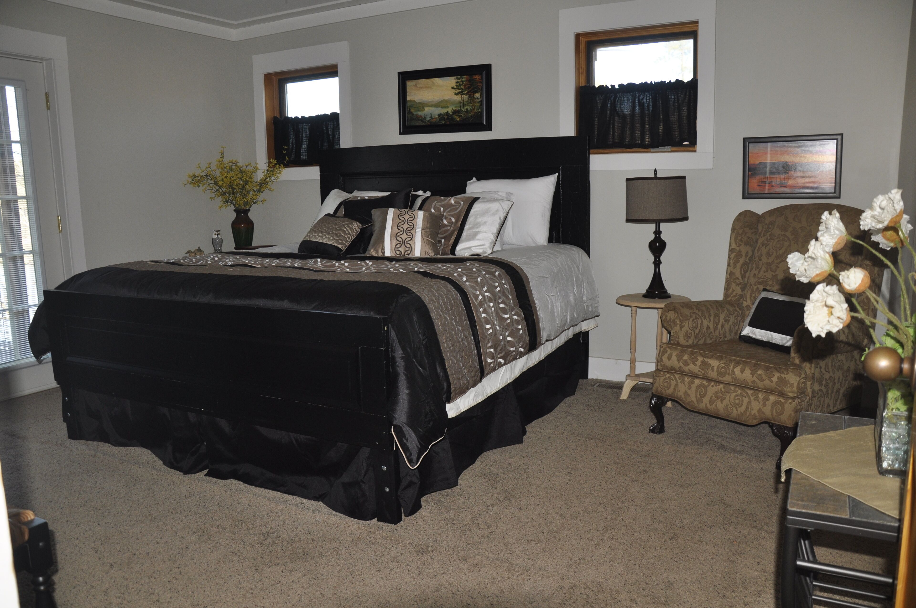 A bedroom with a large bed, a chair, a lamp, and a vase with flowers.
