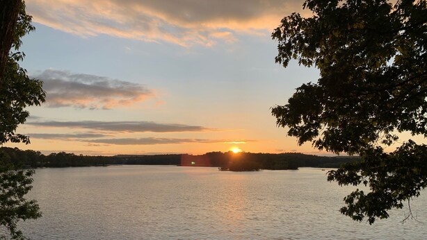 Un lago con un atardecer, un muelle y árboles enmarcándolo.