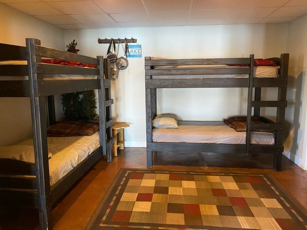 Una habitación con dos literas, un taburete pequeño, un perchero para colgar bolsos y una alfombra de cuadros.