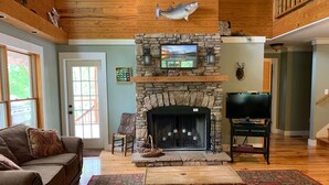 Una sala de estar acogedora con una chimenea de piedra, un televisor y techo de madera.