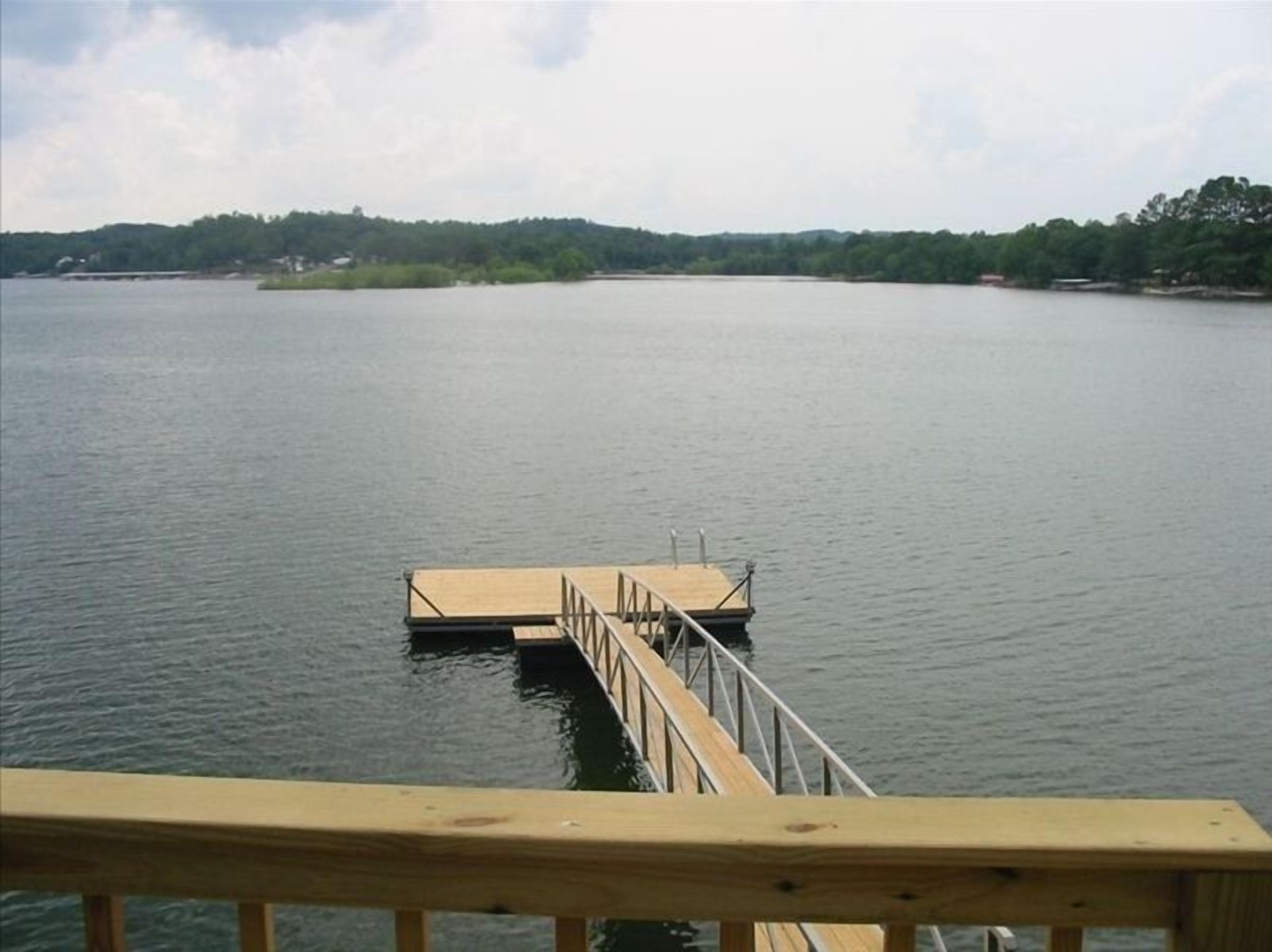 A wooden dock extending into calm water with a forested shoreline in the background.