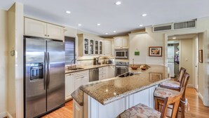 A modern kitchen with stainless steel appliances, granite countertops, and a central island with bar stools. - WOW- New 2bd/2ba, Largest Lanai w/Ocean & Golf Course Views, Lowest Resort Fee! (Lahaina)