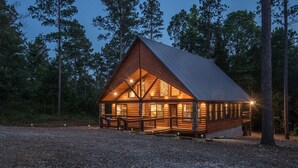 Une cabane en rondins avec des fondations en pierre, de grandes fenêtres et une véranda aménagée avec des sièges.