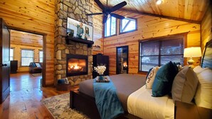 Une chambre confortable dans un chalet en rondins, avec une cheminée en pierre, un grand lit et un ventilateur de plafond.