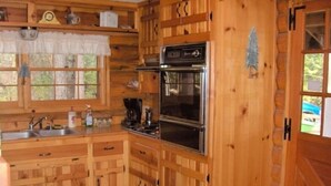 Cocina de cabaña de madera con estufa, horno, pileta y alacenas.