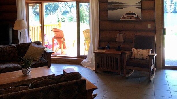 A spacious cabin with a high ceiling and large windows, furnished with a sofa, armchair, and a small table. - Loons Nest - Cozy, secluded 4 bedroom log cabin in the heart of the wilderness! (Tyaughton Lake)