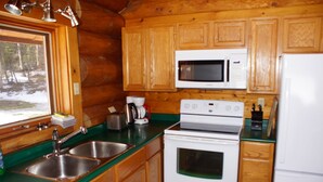 A cabin kitchen with wooden cabinets, a microwave, a stove, and a sink. - Loons Nest - Cozy, secluded 4 bedroom log cabin in the heart of the wilderness! (Tyaughton Lake)
