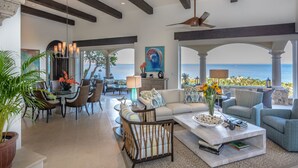 Un vaste espace de vie avec vue sur la mer, comprenant un canapé, des fauteuils, une table basse et un coin repas.