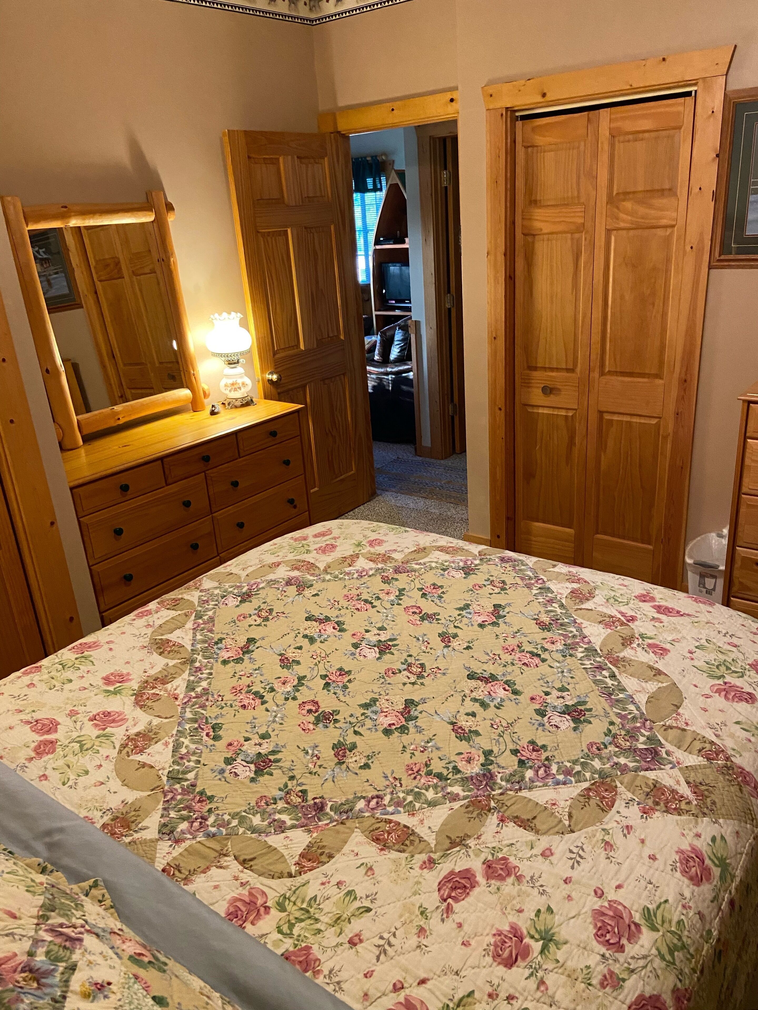 Un dormitori amb llençols estampats de flors, un armari de fusta i una cómoda amb mirall.