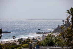 A beach with clear skies, a rocky shoreline, and palm trees.