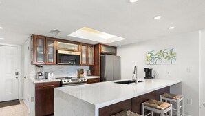 Eine moderne Küche mit Holzausstattung, einer großen Kücheninsel mit Barhocker, einem Kühlschrank und einer Mikrowelle.